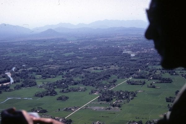 Vietnam countryside seen from a helicopter, soldier’s silhouette in the foreground.