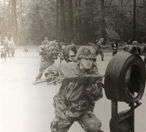 Black and white photo of an Army recruit impairing a mounted tire with a bayonet attached to an M-16 Rifle. The soldier is on the bayonet-training obstacle course