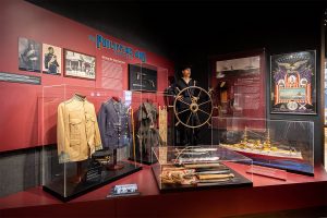 Museum exhibit of sailor behind a wheel, uniforms and weapons