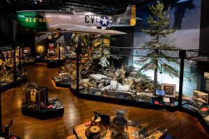 WWII plane over museum galleries with a jeep and soldiers below.