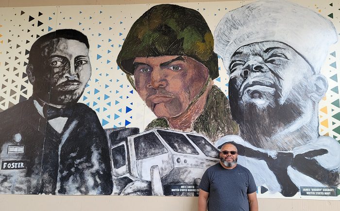 Cocroft standing in front of the Veteran Print Project mural on the exterior of the Wisconsin Veterans Museum, on display 2019 to 2021.