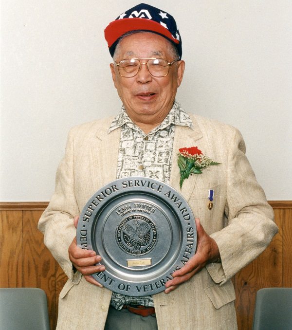 A photograph of Akira Toki holding up his Superior Service Award from the Department of Veterans Affairs for his work at the William S. Middle VA Hospital