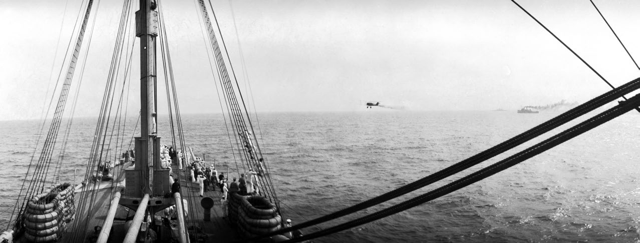 A DH-4 bomber flies low, past the starboard side of USS Henderson (AP-1). Henderson hosted press reporters, military officers, and foreign observers as they observed the 1921 Army-Navy bombing experiments off the Virginia capes. A.W. Smith Collection Naval History and Heritage Command photo.