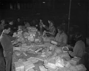 Black women standing at a table sorting packages in a dark warehouse. during WWII. 6888th Central Postal Directory Battalion