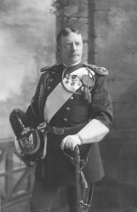 portrait of a man in full dress military uniform, holding a helmet and leaning on a sword