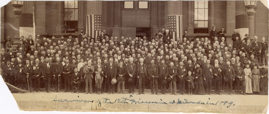 Group image from 1889 of men and women on the steps of a building with US flags.
