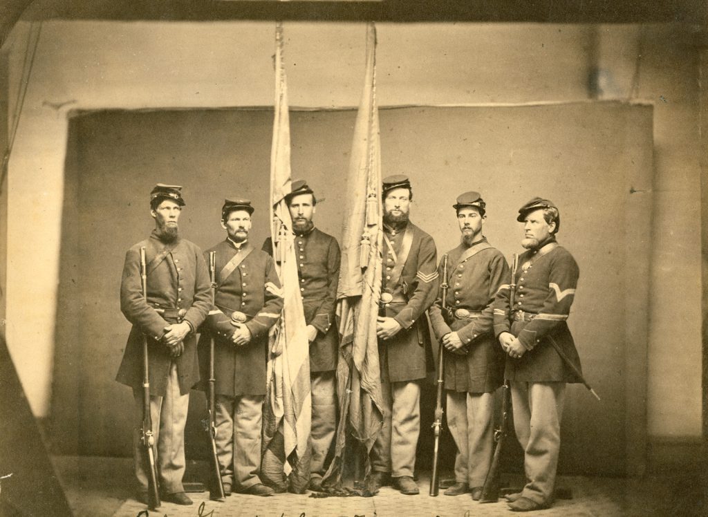 7 men in Union Civil war uniforms holding the national and regimental colors