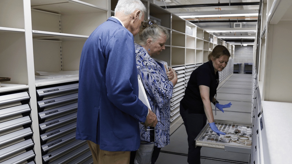 Three people leaning in to view artifacts on a pull out drawer