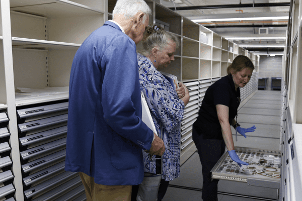Three people leaning in to view artifacts on a pull out drawer