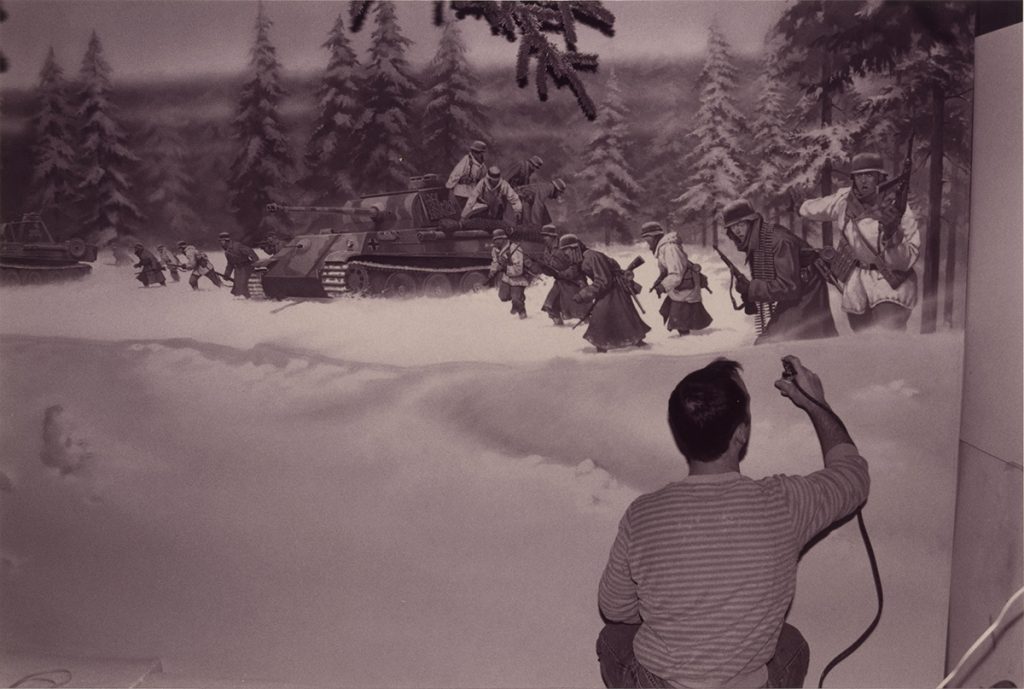 Man painting a mural of a snowy forest with soldiers.