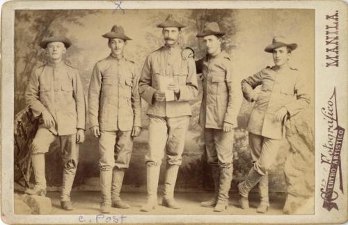  Portrait of 5 soldiers standing in a line, leaning against fake rocks, posed casually in front of a painted backdrop. 
