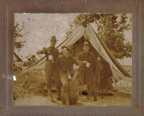 Casual portrait of three soldiers  in front of a tent, presumably drinking alcohol.